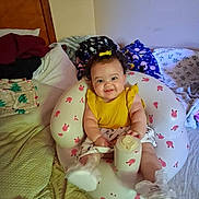 Evanaley is registered to the contest to win money with this photo: baby, infant, child, smiling, sitting, portrait, bedroom, bed, blanket, pillow, clothing, yellow_shirt, hair_bow, bottle, baby_seat, bunny_pattern, indoor, cozy, happy, face