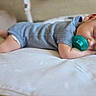 baby, sleeping, pacifier, blue_onesie, infant, bed, white_bedspread, peaceful, cute, newborn, child, resting, indoors, soft_light, portrait, small_feet, head, face, hand, relaxation