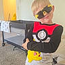 child, boy, pajamas, pikachu, pokemon, sunglasses, indoor, living_room, carpet, baby_crib, blanket, toy, smile, cute, playful, clothing, person, furniture, home, casual