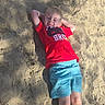 child, boy, sand, sunlight, shadow, relaxed, casual_clothing, outdoor, smiling, red_tshirt, blue_shorts, barefoot, summer, play, leisure, young, portrait, happy, nature, daylight
