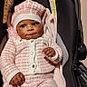 baby, infant, child, car_seat, pink_clothing, hat, knitwear, blanket, cute, portrait, indoors, person, smile, happy, young_child, seated, buttoned_jacket, warm_clothing, face, hands