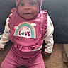 Nevaeh is registered to the contest to win money with this photo: baby, child, infant, pink_clothing, headwrap, bib, rainbow_design, love_text, smiling, seated, couch, indoor, happy, cute, portrait, person, fashion, cozy, young_child, closeup