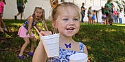 Harley is registered to the contest to win money with this photo: background, blue_dress, butterfly_sticker, child, daylight, event, fun, girl, grass, happy, holding, nature, outdoor, people, plastic_cups, play, portrait, smiling, summer, sunlight