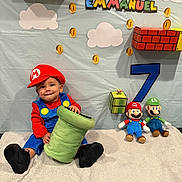 Emmanuel joined the competition — help win amazing prizes! toddler, child, costume, mario, plush_toy, birthday, party_decoration, number_7, soft_blanket, green_pipe, luigi, super_mario, smiling, indoors, decorations, clouds, coins, red_hat, blue_overalls, cute