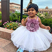 Diya is registered to the contest to win money with this photo: child, toddler, smiling, dress, flower, outdoor, garden, plants, statue, architecture, cloudy_sky, stone_pavement, happy, person, footwear, blue_slippers, nature, greenery, portrait, cute