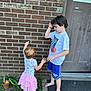 child, toddler, boy, girl, barefoot, brick_wall, door, chalk, grass, potted_plant, shorts, tshirt, outdoor, play, curly_hair, short_hair, side_view, summer, kids, siblings