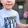 child, boy, face, portrait, tshirt, text, outdoor, person, young, casual_clothing, short_hair, skin, eyes, expression, background, door, blur, colorful, daylight, standing
