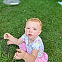 child, toddler, grass, outdoor, greenery, sitting, pink_skirt, short_sleeve_shirt, curly_hair, holding_grass, rosy_cheeks, nature, daylight, cute, portrait, barefoot, summer, playful, young_child, casual_clothes