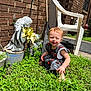 toddler, child, grass, outdoor, sunlight, brick_wall, statue, angel, flowers, plastic_chair, barefoot, greenery, garden, smiling, cute, young_child, nature, daylight, plants, casual_clothing