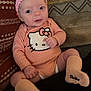 baby, infant, child, pink_headband, hello_kitty, onesie, socks, bambino, couch, cushion, patterned_fabric, smiling, sitting, indoors, cute, portrait, person, apparel, headwear, cozy