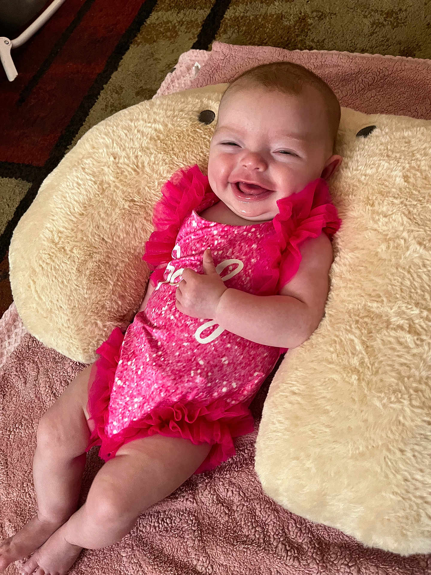 Daniela is registered to the contest to win money with this photo: baby, infant, smiling, pink_dress, fluffy_cushion, blanket, happy, skin, face, child, cute, laying_down, indoors, soft_texture, legs, arm, expression, comfortable, cheerful, toddler