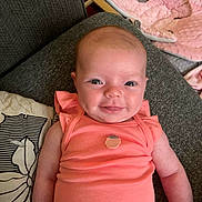 Daniela is registered to the contest to win money with this photo: baby, infant, smile, face, arm, clothing, couch, pillow, fabric, pink, coral, person, indoor, seat, baby_seat, soft_toy, head, skin, cute, happy