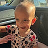 toddler, child, car_interior, sunlight, smiling, onesie, playful, hand, window, seat, seatbelt, face, head, hair, clothing, expression, indoor, daylight, person, cute