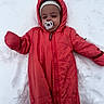 baby, child, cold, cozy, cute, face, gloves, hood, infant, lying_down, one_person, outdoor, pacifier, red_clothing, smiling, snow, snowsuit, snowy_ground, winter, winter_clothing