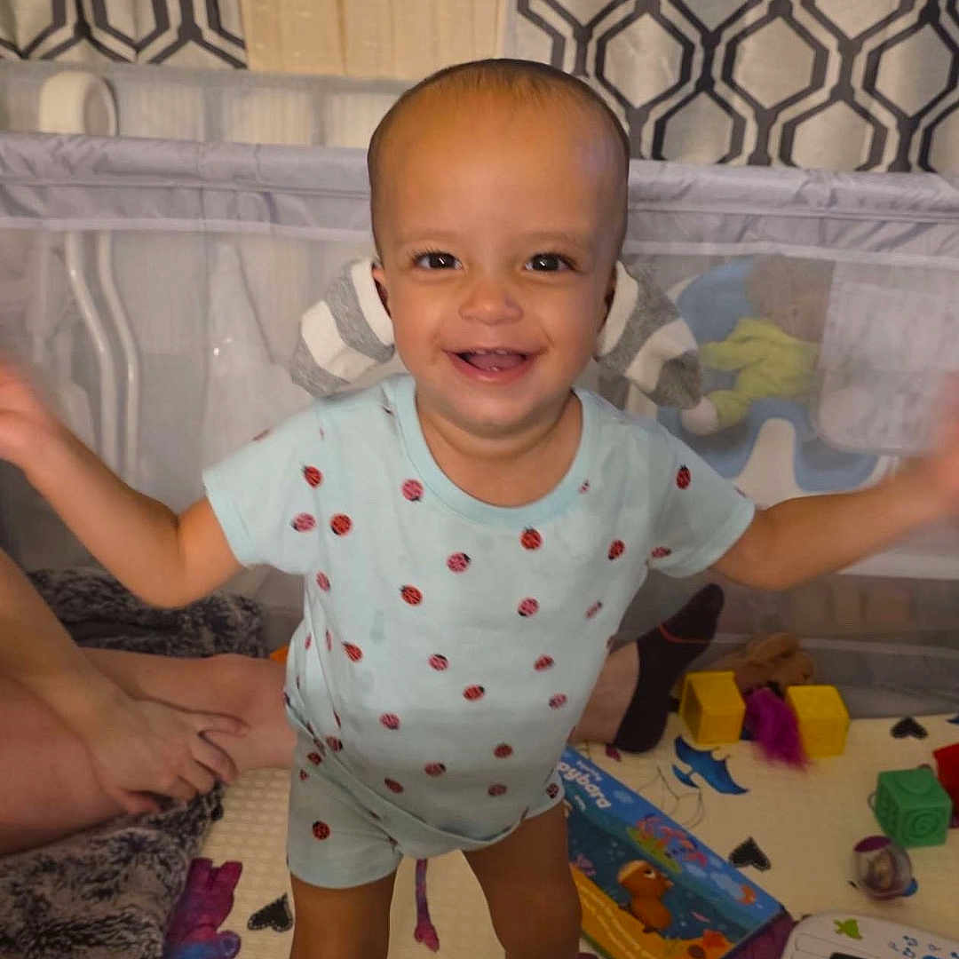 Zemira is registered to the contest to win money with this photo: toddler, child, baby, smiling, standing, portrait, crib, nursery, toy, keyboard, play_mat, colorful, indoors, happy, face, clothing, barefoot, infant, patterned_background, family