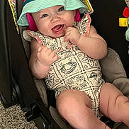 Paige is registered to the contest to win money with this photo: baby, infant, smiling, hat, bucket_hat, romper, baby_carrier, carpet, happy, cute, child, skin, face, arm, leg, foot, patterned_clothing, indoor, playful, joyful