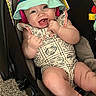 baby, infant, smiling, hat, bucket_hat, romper, baby_carrier, carpet, happy, cute, child, skin, face, arm, leg, foot, patterned_clothing, indoor, playful, joyful