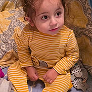 Brando joined the competition — help win amazing prizes! toddler, child, curly_hair, yellow_onesie, striped_clothing, sitting, indoors, bed, blanket, toy, baby_bottle, cute, soft_lighting, curious_expression, face, person, cozy, home, infant, young_child
