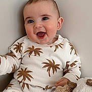 Jace is registered to the contest to win money with this photo: baby, child, smiling, pajamas, palm_tree_pattern, stuffed_animal, plush_toy, happy, indoors, person, cute, infant, face, portrait, seated, cozy, clothing, young_child, soft_toy, wall