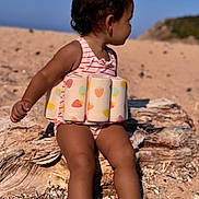 Alba a rejoint le concours — aidez-le/la à gagner de superbes lots ! toddler, child, beach, swimsuit, floatation_device, sand, driftwood, sunlight, outdoor, barefoot, summer, water_safety, nature, vacation, sea, sky, sunny, relaxing, side_view, young_child