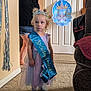 Maria is registered to the contest to win money with this photo: child, birthday, princess, tiara, sash, dress, carpet, indoor, person, adult, door, party, celebration, sock, blue, purple, home, decoration, target, happy