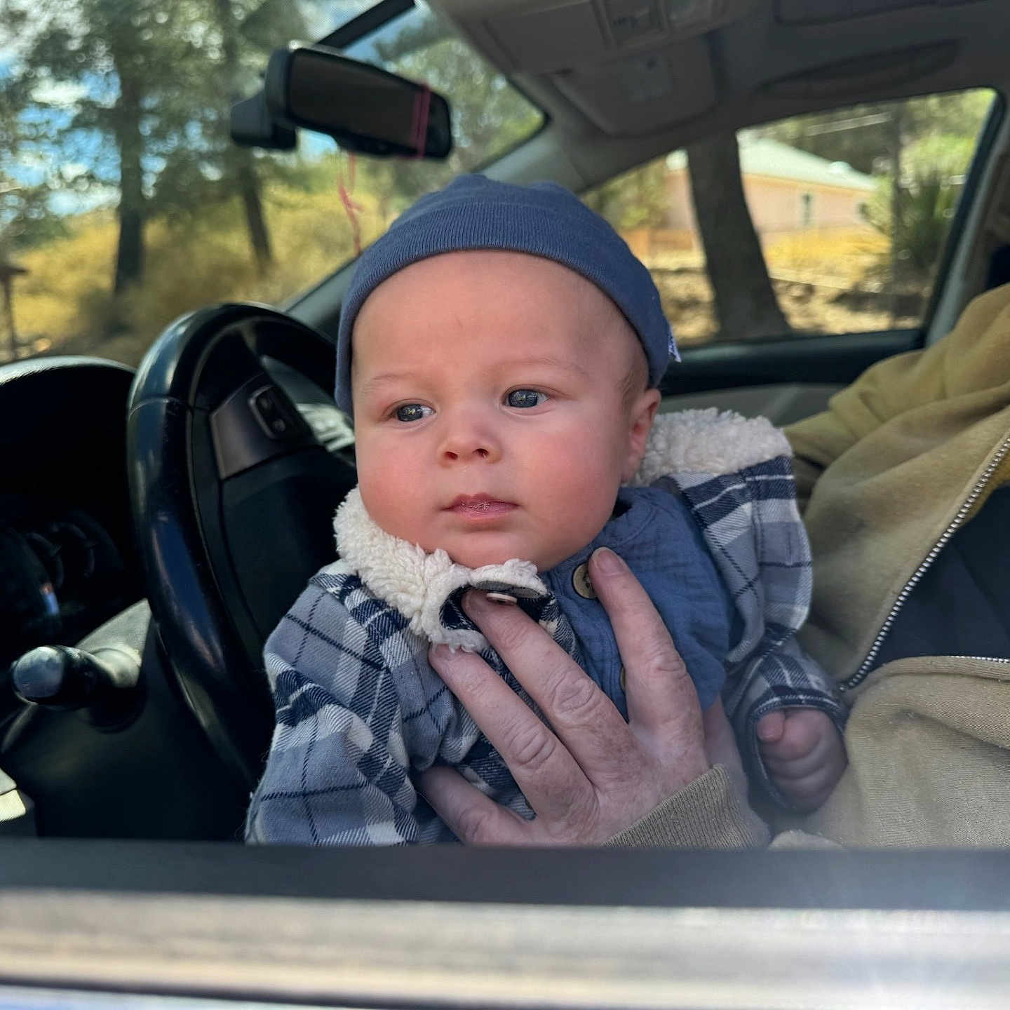 Dean is registered to the contest to win money with this photo: adult, baby, blue_beanie, car_interior, child, clothing, cozy, face, hand, house, infant, outdoor, person, plaid_jacket, portrait, seat, steering_wheel, sunlight, trees, window