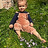 barefoot, casual_clothing, child, corduroy, daylight, flowers, garden, grass, greenery, happy, nature, outdoor, overalls, playful, portrait, sitting, smile, sunlight, toddler, young_child