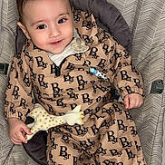 Gianny a rejoint le concours — aidez-le/la à gagner de superbes lots ! baby, child, infant, pacifier, toy, giraffe, clothing, seat, patterned, smiling, happy, sitting, cute, indoor, floor, footwear, onesie, fabric, person, portrait