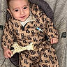 baby, child, infant, pacifier, toy, giraffe, clothing, seat, patterned, smiling, happy, sitting, cute, indoor, floor, footwear, onesie, fabric, person, portrait