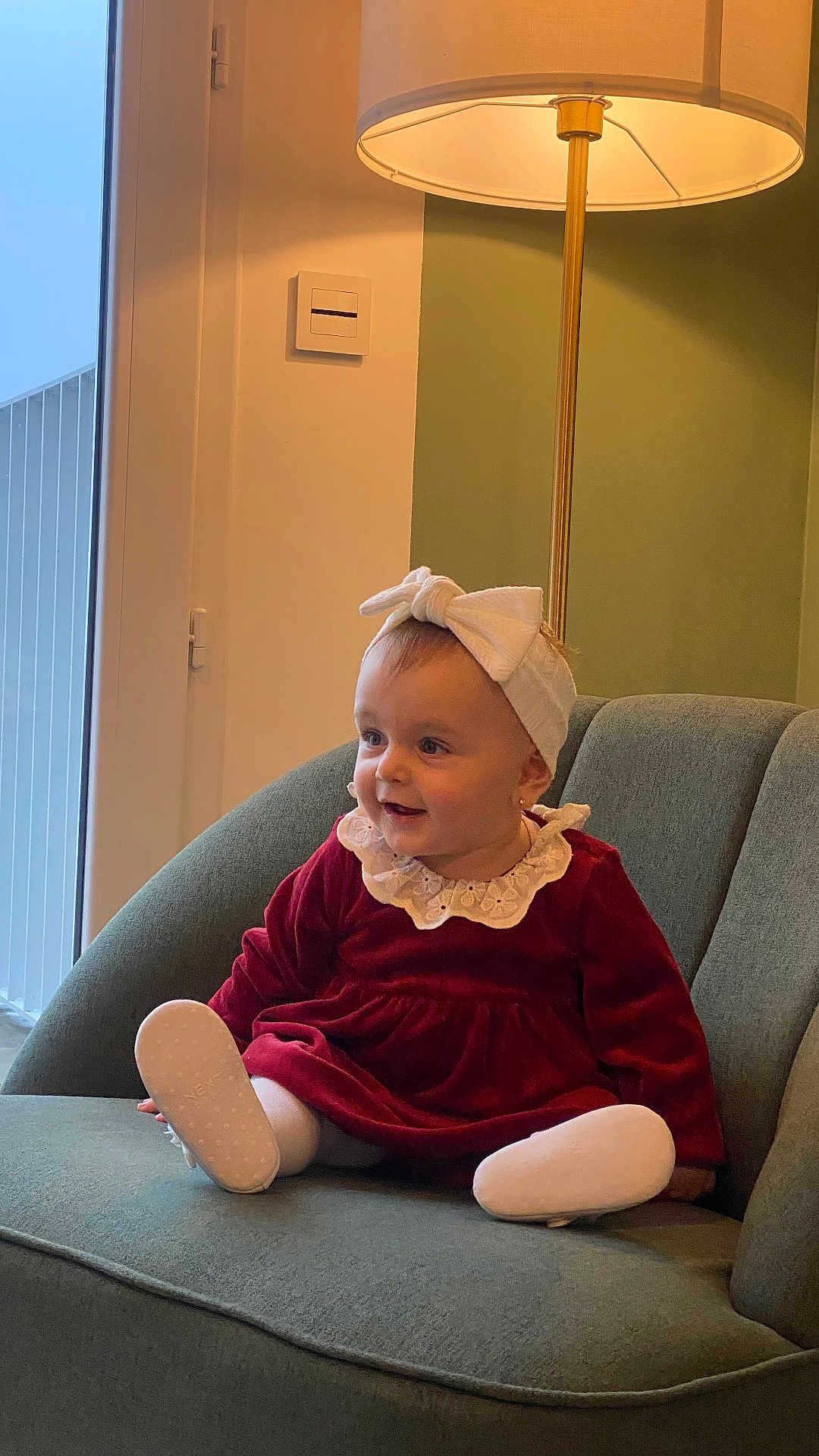 Jane participe au concours pour gagner de l'argent avec cette photo : baby, child, girl, red_dress, headband, bow, armchair, lamp, indoor, smile, happy, toddler, white_tights, footwear, furniture, portrait, cute, cozy, home, fashion