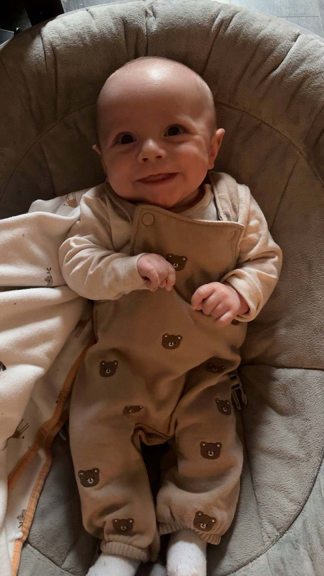 Enzo is registered to the contest to win money with this photo: apparel, baby, bear_pattern, blanket, child, cozy, cushion, cute, happy, indoors, infant, overalls, person, plush, portrait, relaxed, seat, smiling, soft_lighting, white_socks