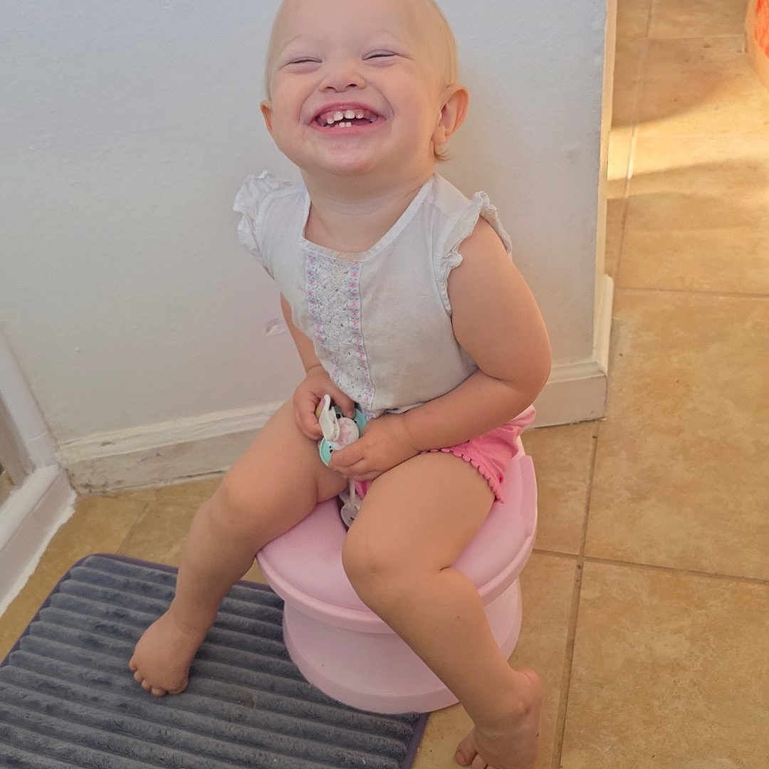 Vylette is registered to the contest to win money with this photo: toddler, child, smile, potty, bathroom, floor, tile, mat, pink, white_shirt, shorts, happy, sitting, barefoot, indoor, light, sunlight, young_child, cute, joy