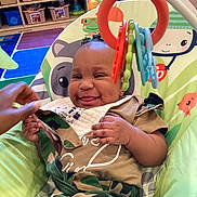 Emmani joined the competition — help win amazing prizes! baby, baby_chair, bib, child, clothing, colorful, cute, early_childhood, expression, face, furniture, hand, happy, indoor, infant, person, play, playroom, smiling, toy