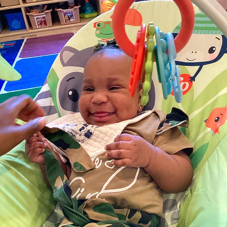 Emmani joined the competition — help win amazing prizes! baby, baby_chair, bib, child, clothing, colorful, cute, early_childhood, expression, face, furniture, hand, happy, indoor, infant, person, play, playroom, smiling, toy