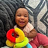 Emmani is registered to the contest to win money with this photo: baby, blanket, child, colorful, couch, cozy, cute, face, happy, home, indoors, infant, person, pink_clothing, playful, plush_toy, seated, smiling, soft_texture, toy