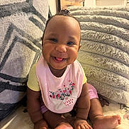 Emmani joined the competition — help win amazing prizes! baby, smiling, sitting, indoors, blanket, cushion, cozy, happy, child, pink_bib, yellow_shirt, cute, portrait, home, infant, foot, hand, skin, hair_tie, expression