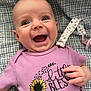 baby, smiling, purple_shirt, sunflower, glitter, blanket, checkered_pattern, happy, infant, cute, hand, face, portrait, clothing, toddler, lying_down, expression, child, indoors, closeup