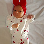 Thalya participe au concours pour gagner de l'argent avec cette photo : baby, infant, red_bow, white_outfit, apple_prints, red_socks, lying_down, blanket, cute, newborn, child, portrait, indoors, clothing, headwear, fist, expression, soft_light, fabric, resting