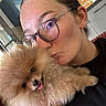 Mia participe au concours pour gagner de l'argent avec cette photo : woman, glasses, dog, pomeranian, pet, cute, fluffy, tongue_out, kiss, selfie, indoor, kitchen, watch, black_clothing, hair_tied_back, face, hand, cuddling, happy, home