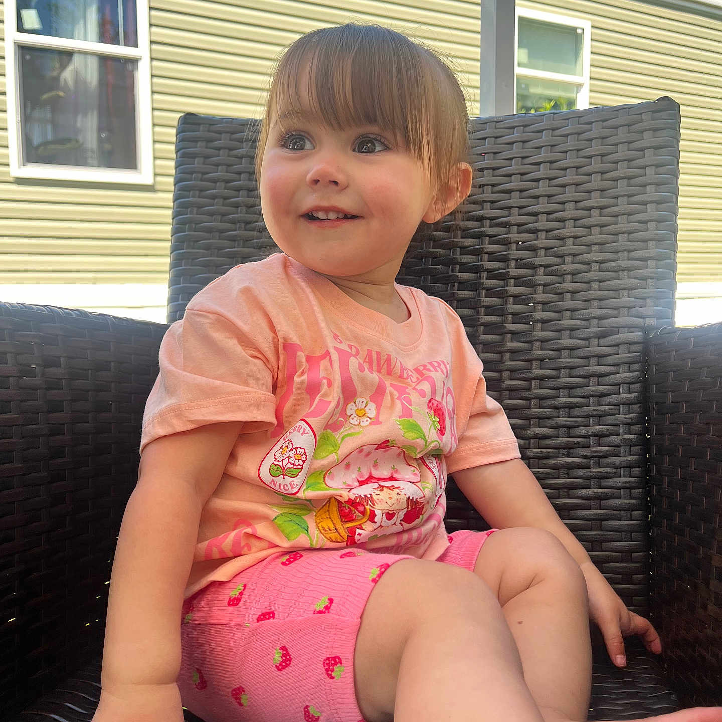 Oaklynn is registered to the contest to win money with this photo: toddler, child, smiling, outdoor, wicker_chair, pink_clothing, shorts, tshirt, sunlight, happy, face, person, summer, nature, greenery, window, mobile_home, sitting, casual, cute