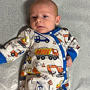 Blake is registered to the contest to win money with this photo: baby, infant, onesie, construction_theme, blue_trim, pacifier, lying_down, gray_background, cute, clothing, child, face, small_hands, foot, soft_surface, indoor, expression, patterned_clothing, newborn, resting