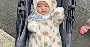 Orhan is registered to the contest to win money with this photo: baby, infant, stroller, onesie, knit_hat, heart_pattern, baby_clothing, footwear, sidewalk, outdoor, baby_bib, cute, bundle_up, gray_stroller, baby_face, person, child, winter_clothing, baby_accessory, urban