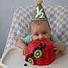 Nikolai is registered to the contest to win money with this photo: baby, child, high_chair, party_hat, watermelon, blueberries, kiwi, fruit, food, celebration, half_birthday, checkered_cloth, table, cute, smiling, indoor, portrait, infant, person, eating