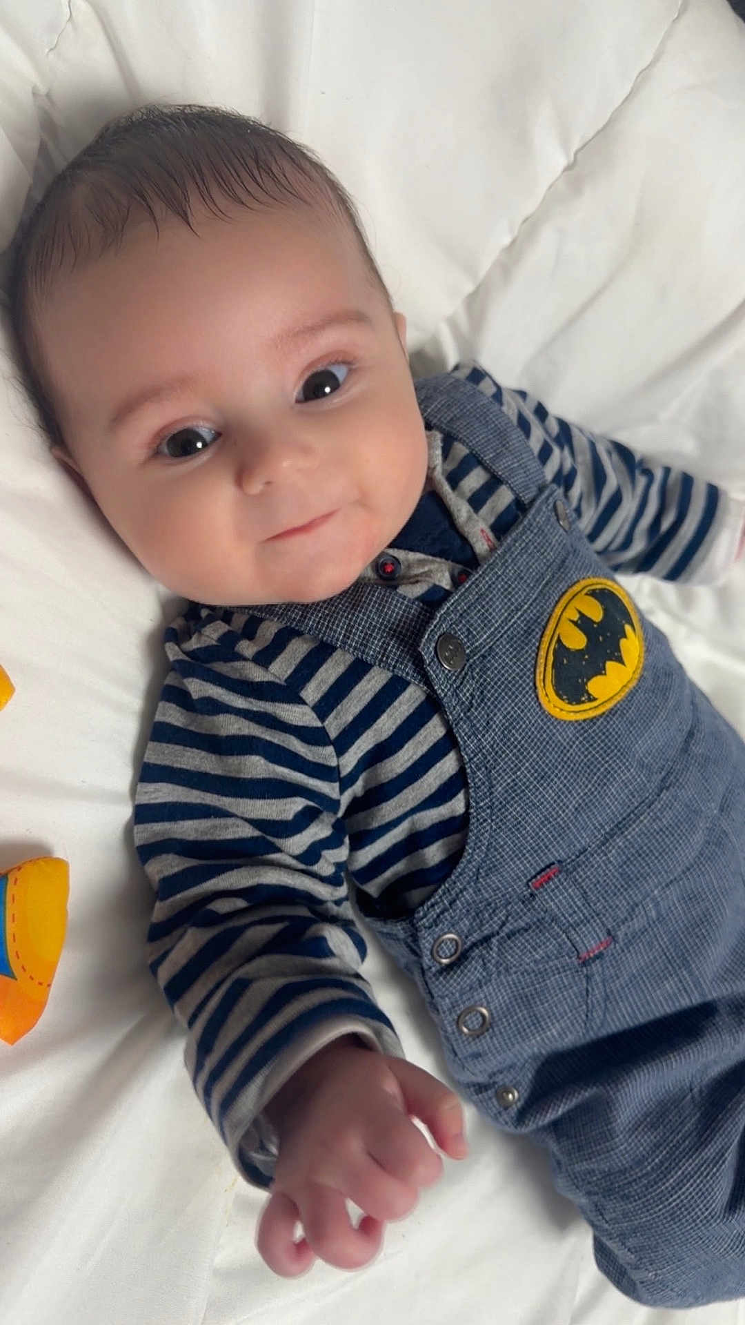 Mylann participe au concours pour gagner de l'argent avec cette photo : baby, infant, child, face, eyes, smile, overalls, batman_patch, striped_shirt, denim, button, hand, lying_down, bedding, blanket, portrait, cute, cozy, looking_at_camera, small_hands