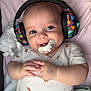 adorable, baby, blanket, blue_eyes, child, colorful, comfort, cute, face, hands, headphones, indoors, infant, lying_down, pacifier, plush_toy, resting, sleepwear, smiling, soft_toys