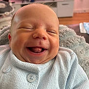 Logan joined the competition — help win amazing prizes! baby, smiling, laughing, infant, knitted_sweater, blue_clothing, face, tongue, closed_eyes, blanket, cozy, indoors, home, furniture, soft_texture, cute, happy, person, portrait, child