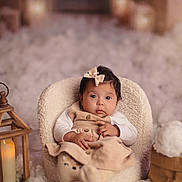 Hinaya a rejoint le concours — aidez-le/la à gagner de superbes lots ! baby, infant, child, bow, dress, chair, lantern, candle, soft_texture, fluffy, cozy, indoor, portrait, cute, expression, warm_light, decor, sitting, winter_theme, curious