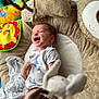 baby, infant, smiling, laughing, cushion, bear_shape, toy, colorful, blanket, white_clothing, soft_texture, indoor, floor, play_area, child, happy, cute, newborn, person, toddler