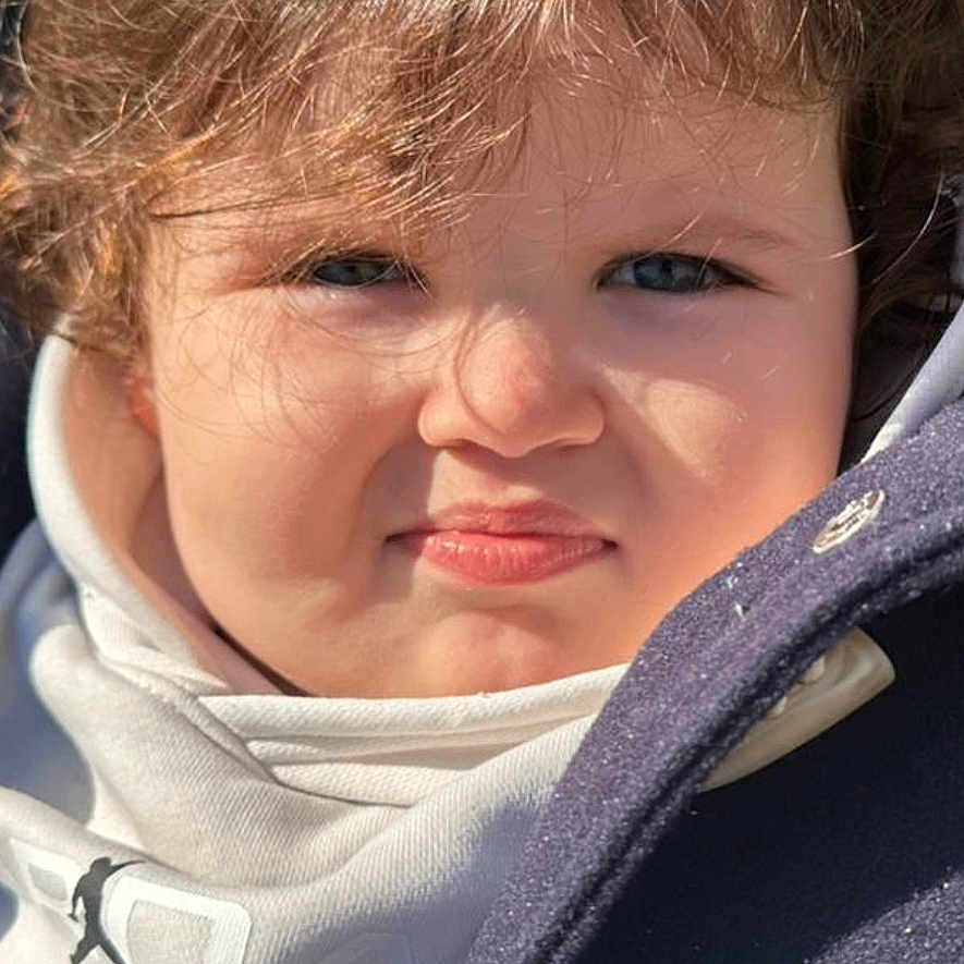 Nazim a rejoint le concours — aidez-le/la à gagner de superbes lots ! toddler, child, face, curly_hair, hoodie, coat, squinting, expression, outdoor, sunlight, portrait, young_child, cute, clothing, person, closeup, funny_face, casual_wear, winter_wear, baby