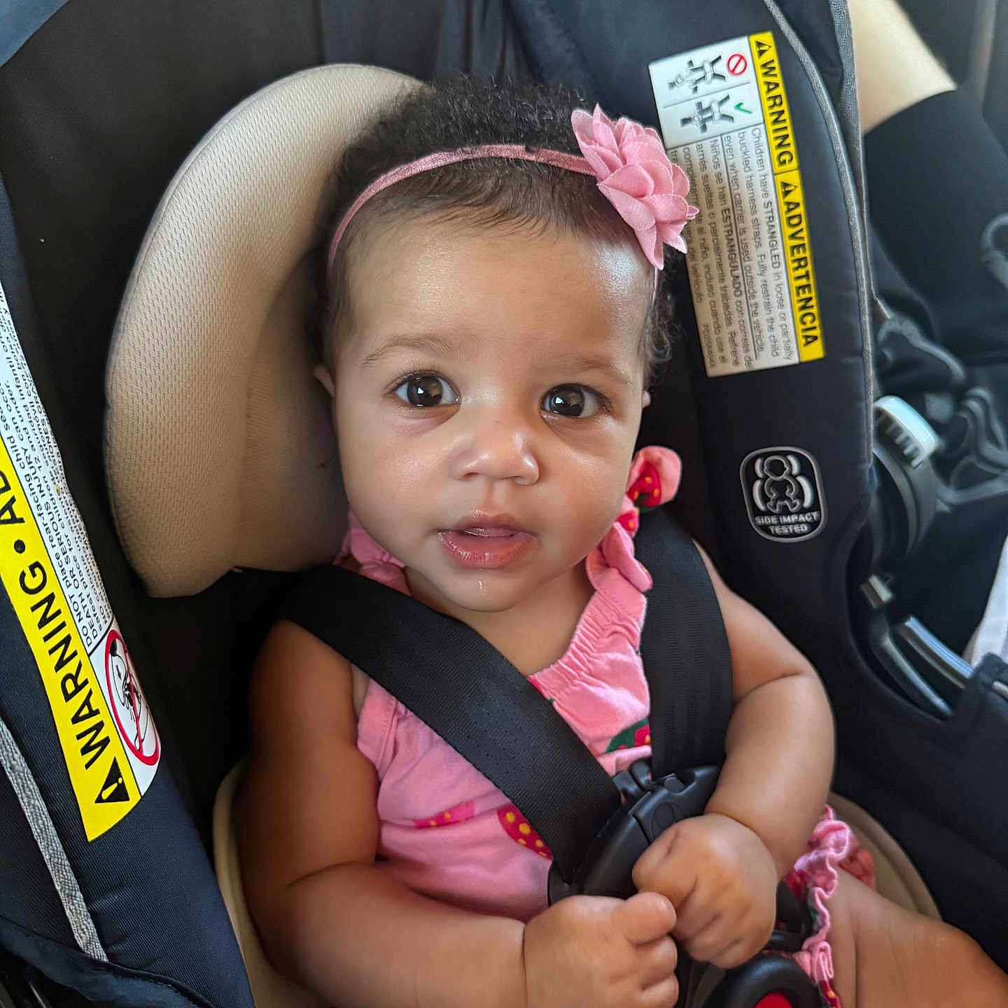 Iris is registered to the contest to win money with this photo: baby, car_interior, car_seat, child, closeup, cute, drool, expression, eyes, face, hands, infant, pink_clothing, pink_headband, portrait, safety, seat, seatbelt, warning_label, young_child
